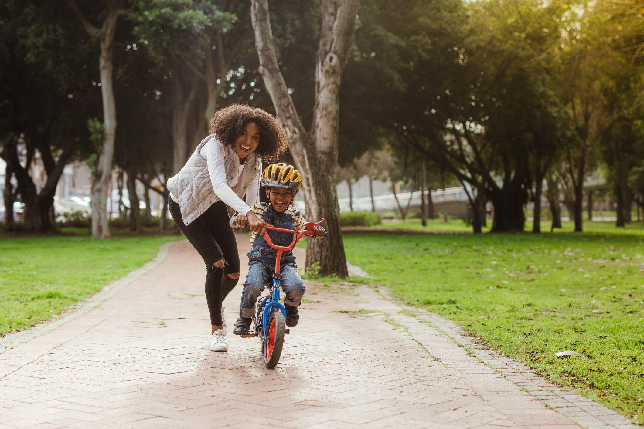 Cute boy learning to ride a bicycle with his mother. Woman teaching son to ride bicycle at park.